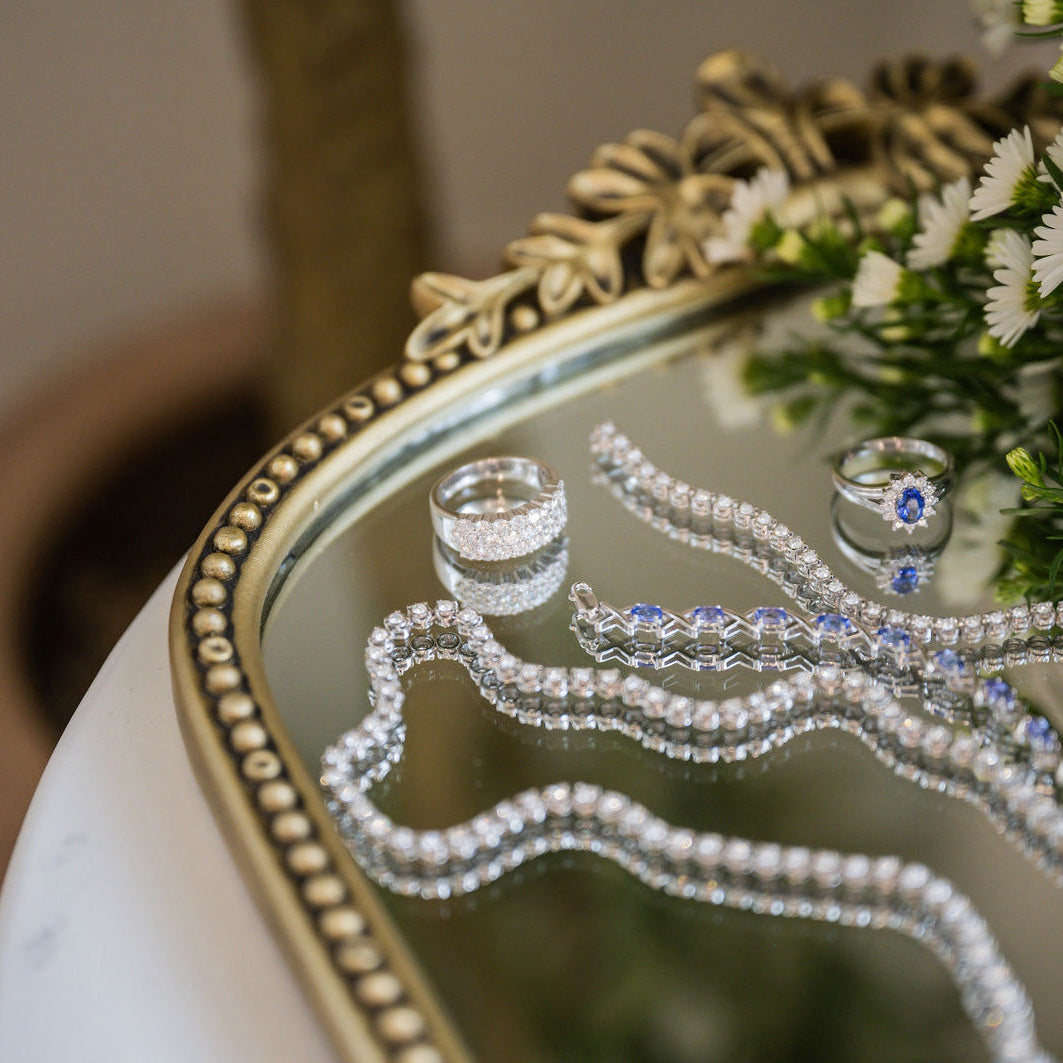 Diamond necklaces, rings, and bracelets on a mirrored antique tray next to flowers, symbolizing diamond certification