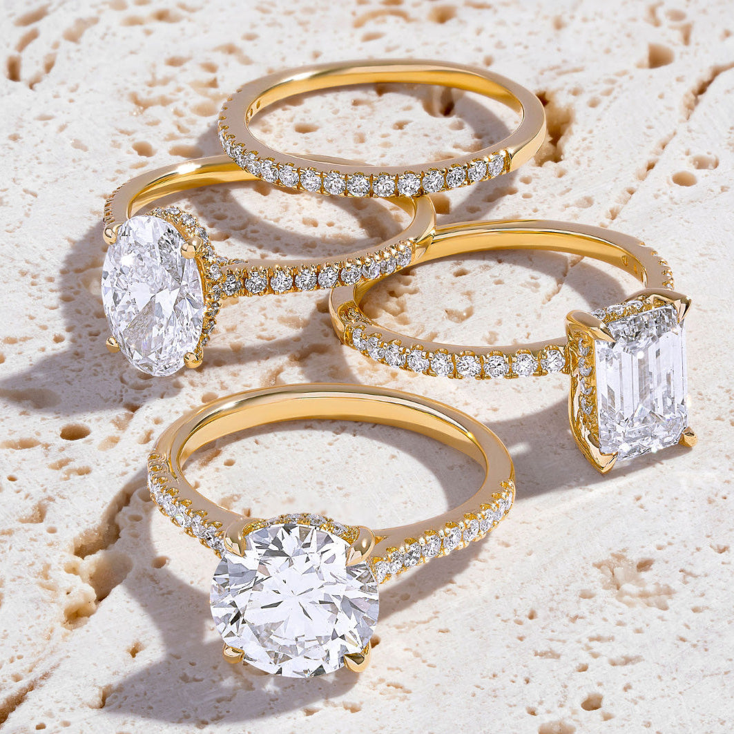 Four diamond rings, including three solitaire engagement rings arranged on a light, textured surface