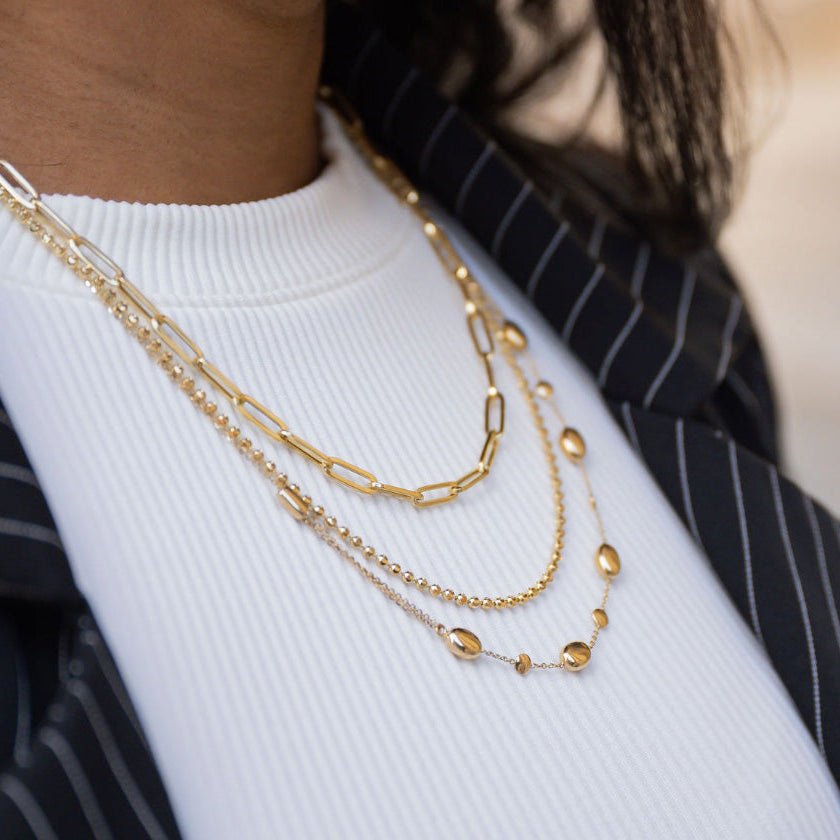 Profile view of a woman wearing three strands of yellow gold jewelry necklaces and diamond hoop earrings