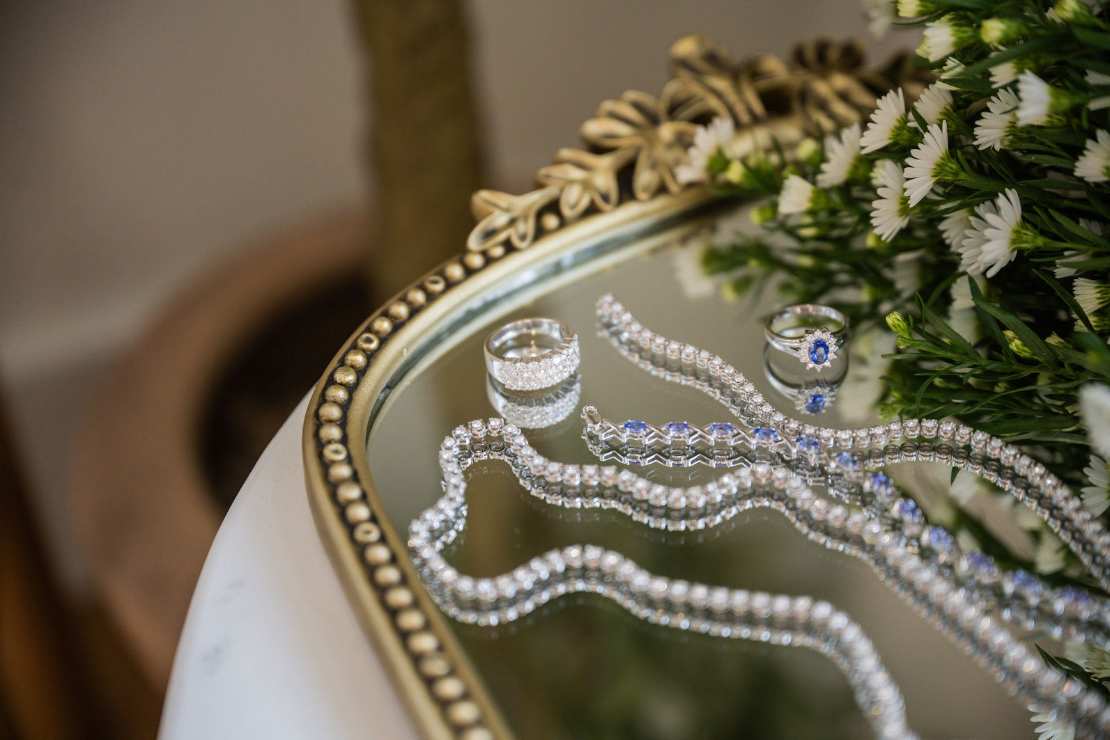 Diamond necklaces, rings, and bracelets  on a mirrored antique tray next to flowers, symbolizing diamond certification