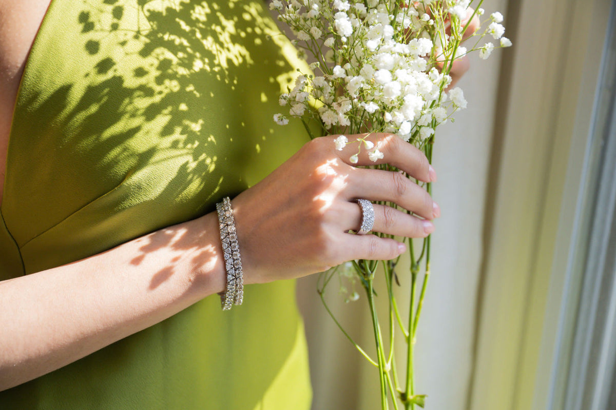 Faceless woman in green dress wearing two tennis bracelets and a three row diamond ring, holding a bouquet of baby’s breath