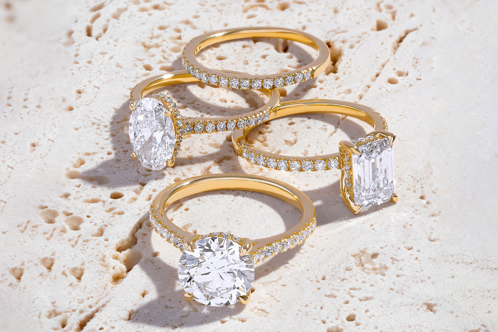 Four diamond rings, including three solitaire engagement rings arranged on a light, textured surface