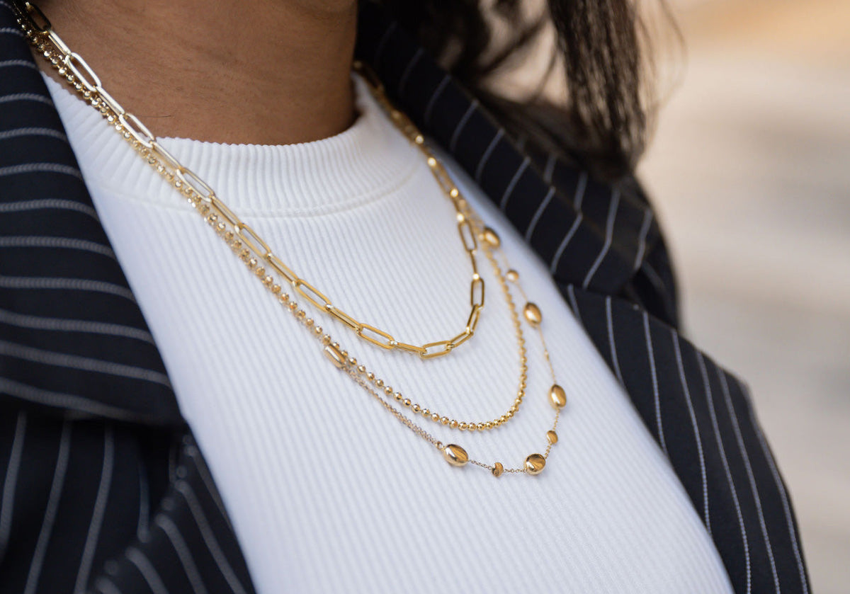 Profile view of a woman wearing three strands of yellow gold jewelry necklaces and diamond hoop earrings