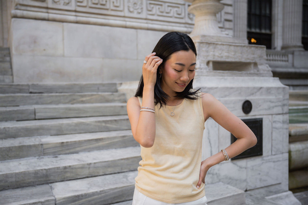 Woman outside of a building, smiling and tucking her hair behind her ear while wearing jewelry for everyday wear