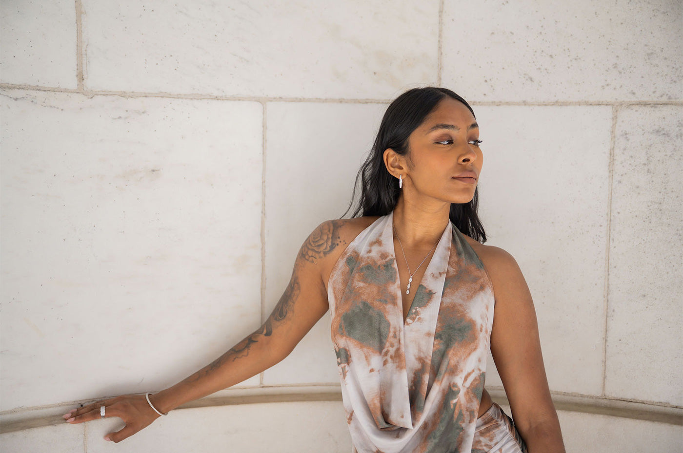Woman wearing white gold Milano bracelet, ring, earrings, and necklace while leaning against a white marble wall